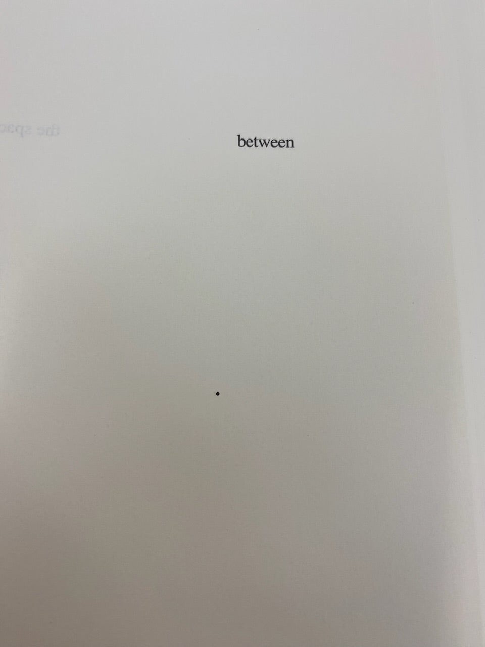an image of a page of the book House of Leaves. There’s a random black dot on a mostly empty page, a fair bit below the word “between”.