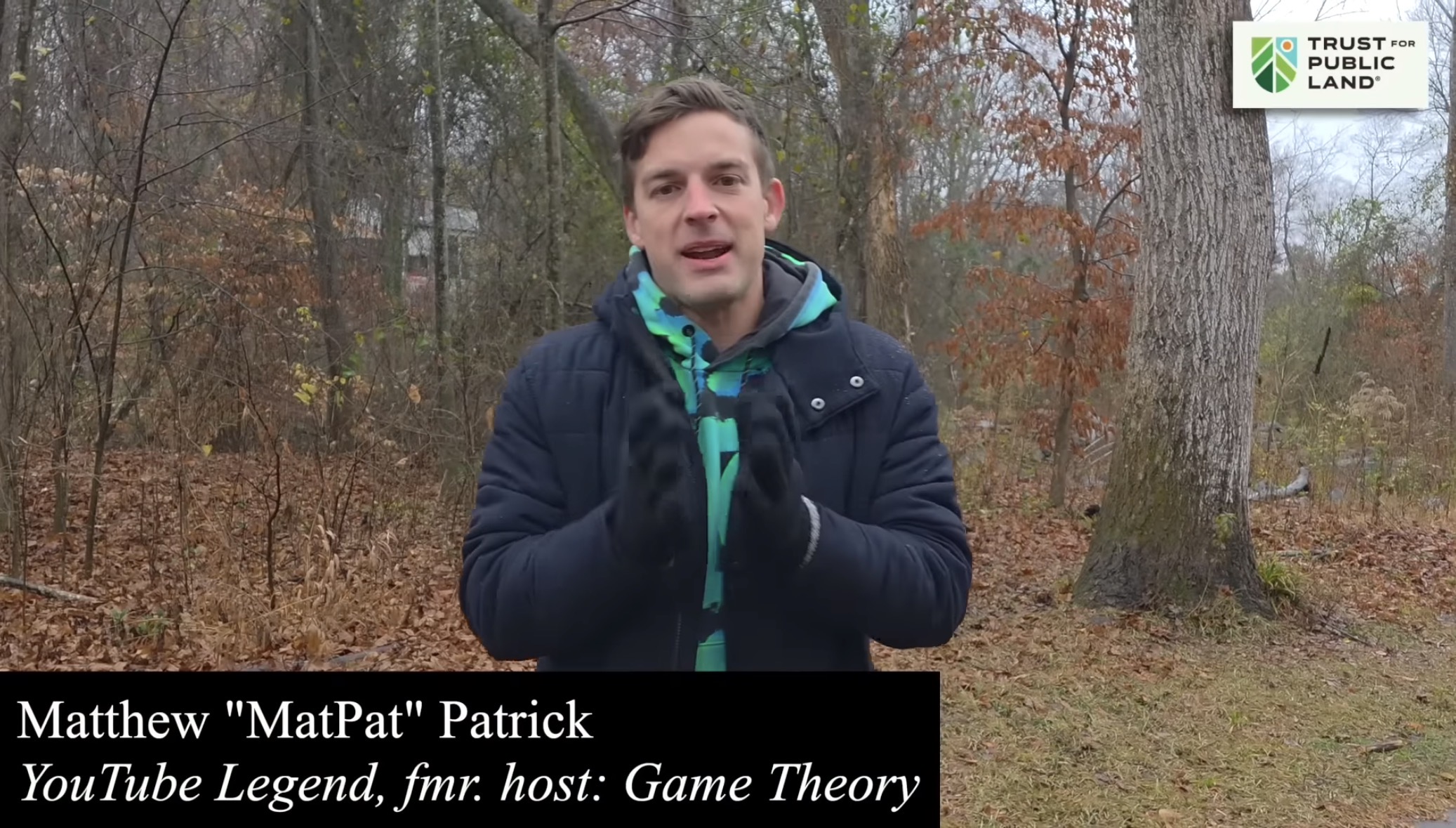 Matpat wearing a dark jacket and gloves gestures with his hands in a leaf-covered forest. Text reads: Matthew "MatPat" Patrick  YouTube Legend, fmr. host: Game Theory